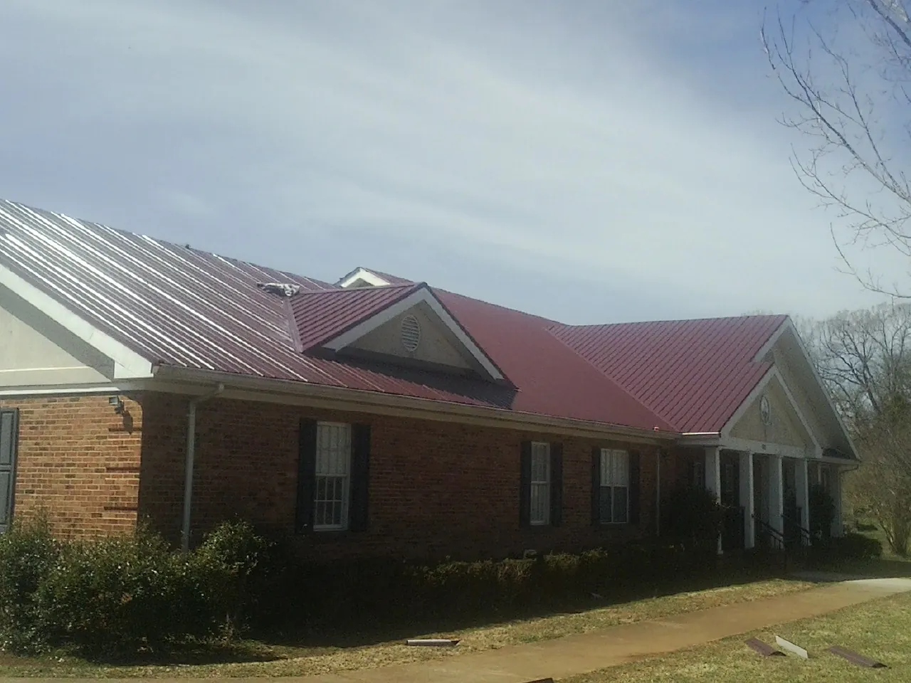 Red metal roof with gabled entries on a long brick building, from a Hail Damage Roof Repair job in Sedalia