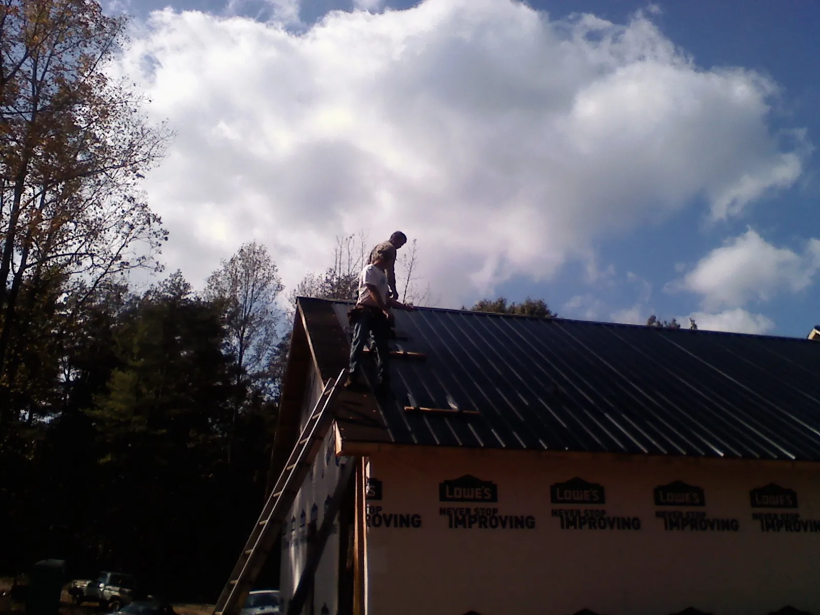 Roofer fastening dark metal panels high against a cloudy sky, from a Roof Inspection job in Sedalia