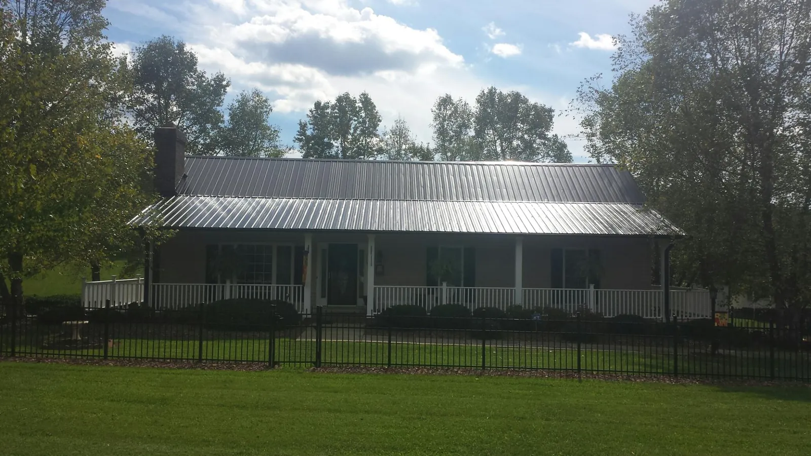 Gray metal roof on a brick ranch with a full width front porch — Gutter Guard Installation work by our crew in Sedalia