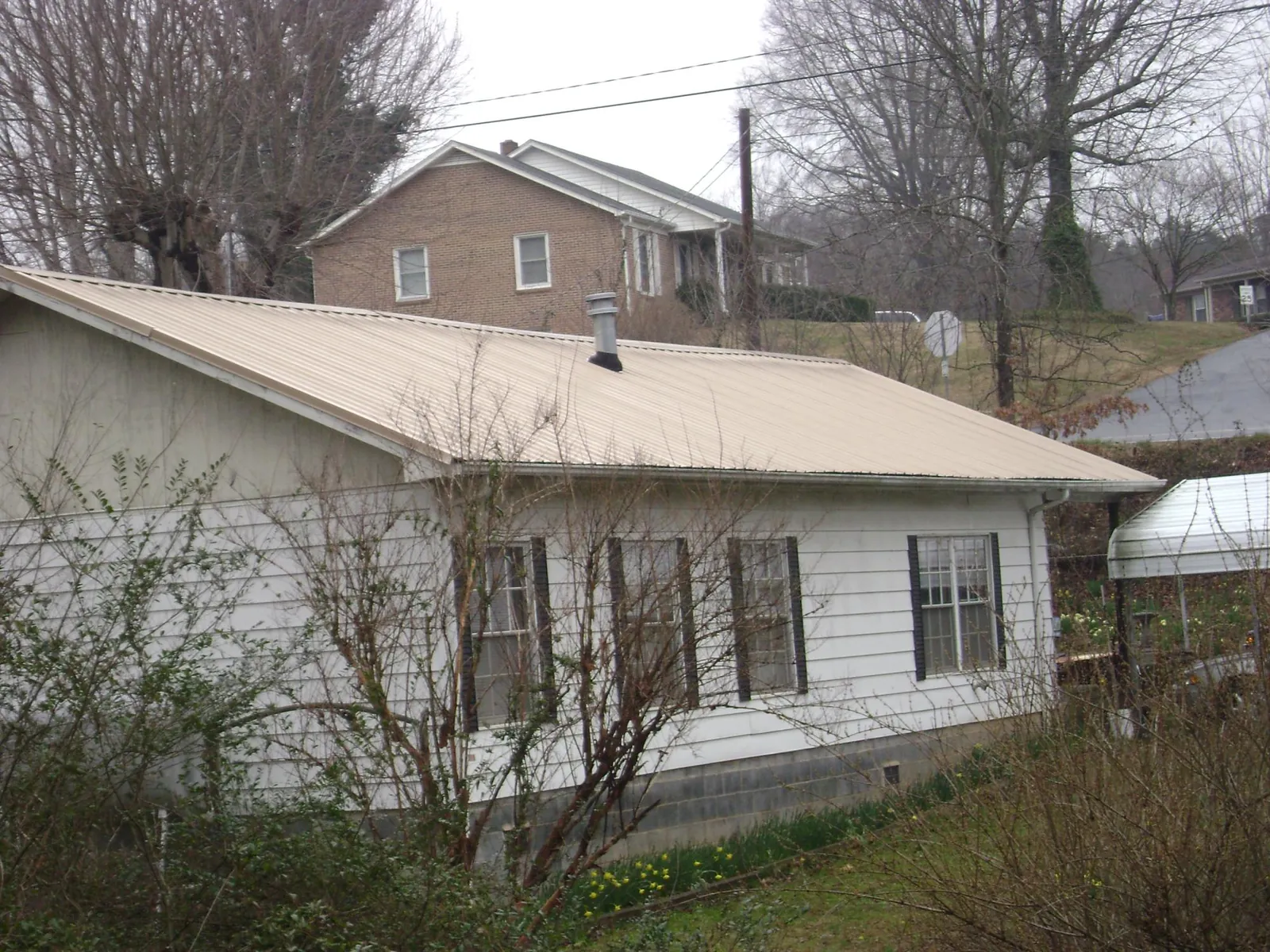 Tan metal roof on a white sided house set into a hillside — Commercial Roofing by Roofing Brothers in Sedalia